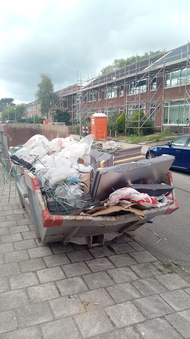 Skip bin of building waste outside scaffolded houses