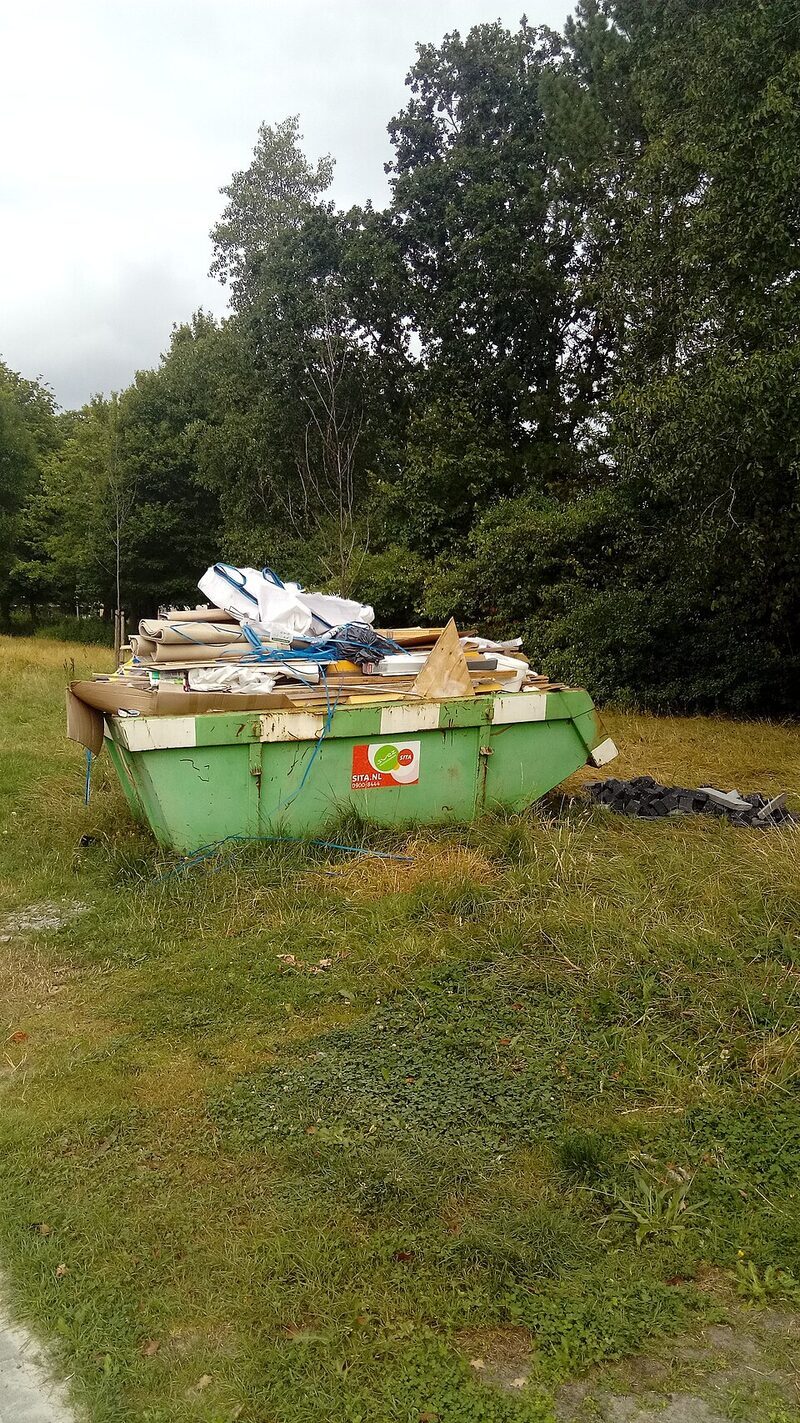 Green skip bin overflowing with renovation waste in a field