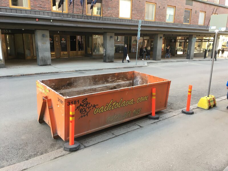 Empty orange 6 cubic metre mid skip bin placed on a city street with safety bollards