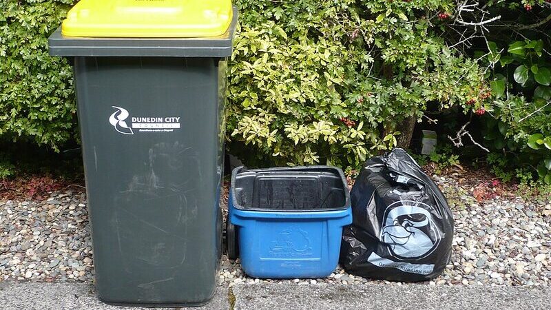 Kerbside wheelie bin with a single rubbish bag waiting beside it
