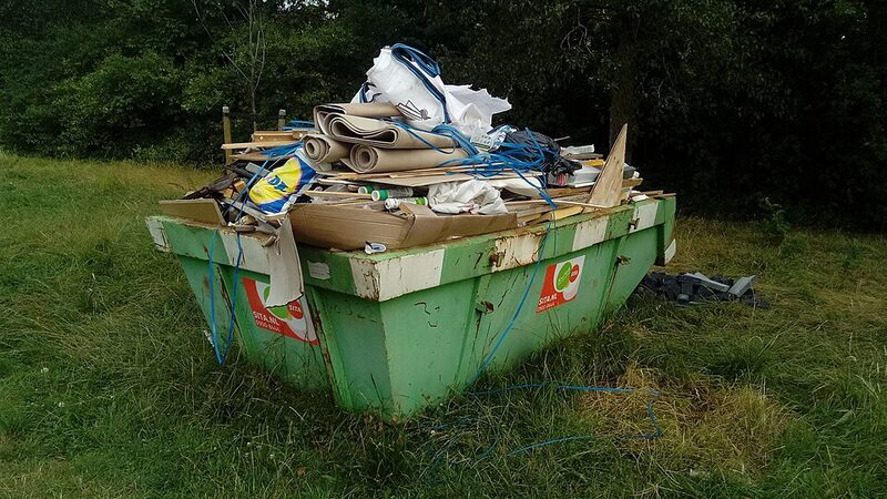 Green skip bin packed with mixed household rubbish, close view
