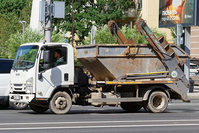 White Isuzu skip-loader truck carrying a steel skip bin on the road