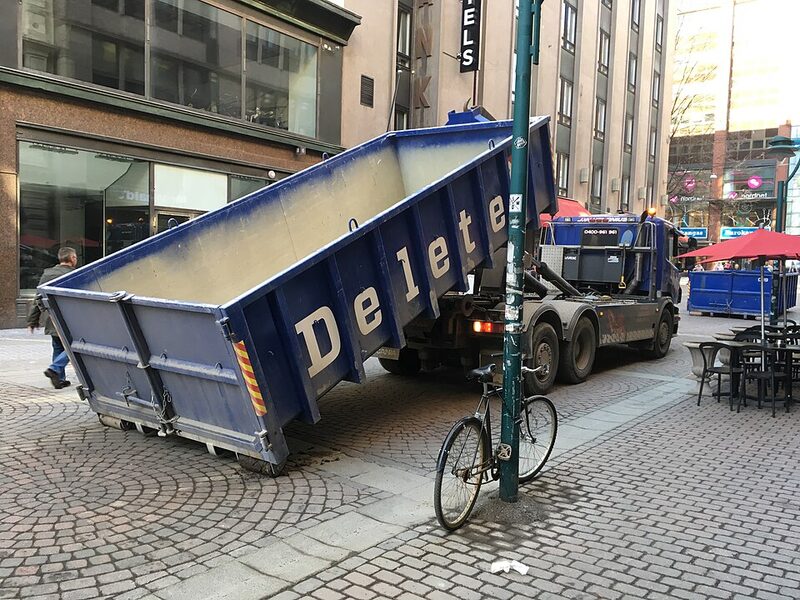 Blue hook-lift truck unloading a skip container on a city street